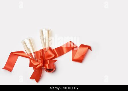 two champagne flutes wrapped in red satin ribbon on a white background with copy space for your text or message to be Stock Photo