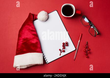 a santa hat, eyeglasses and pen on a red background with a cup of coffee next to it Stock Photo