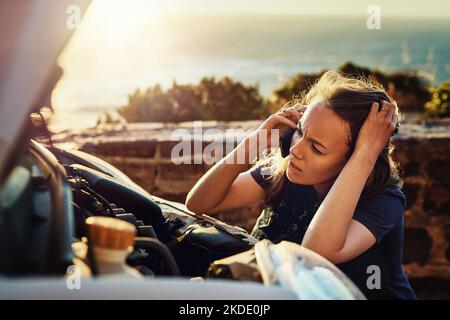 Car problems are so frustrating. a young woman calling roadside assistance after breaking down. Stock Photo