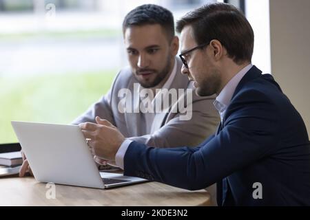 Teammates look at laptop screen, discuss on-line project Stock Photo