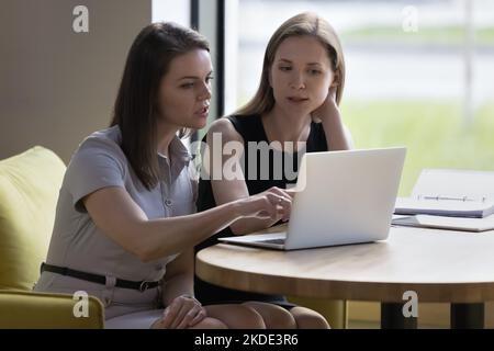 Two businesswomen learn collaborative task looking at laptop screen Stock Photo