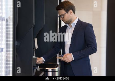 Businessman in suit pours coffee uses vending machine in office Stock Photo