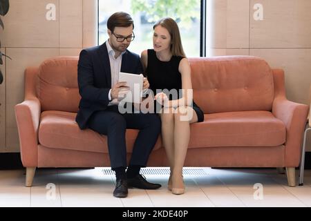 Workmates using digital tablet working seated on sofa in workspace Stock Photo