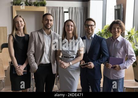 Five employees standing in office posing together for company photo Stock Photo