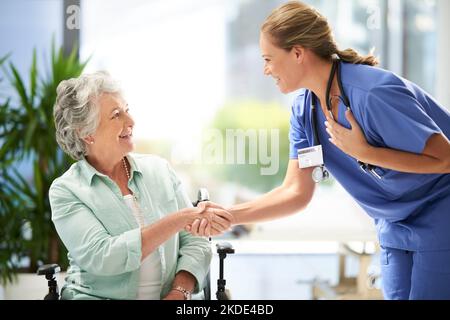 Im gonna take good care of you. an attractive female nurse shaking hands with her wheelchair-bound senior patient in the hospital. Stock Photo