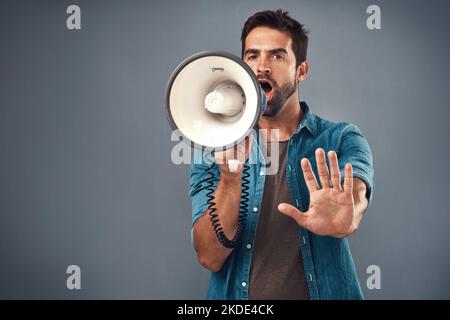 Speak up in the name of justice. Studio shot of a handsome young man using a megaphone against a grey background. Stock Photo