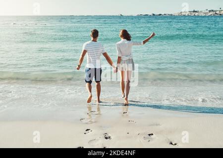 Beach days are barefoot days. Rearview shot of an unrecognizable and carefree young couple running along the beach. Stock Photo