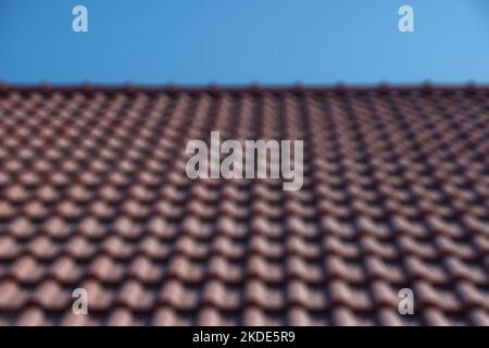 Abstract defocused blured background Brown tile roof under blue sky. The photo is divided on two part. One part is a roof made of clay tiles and the Stock Photo