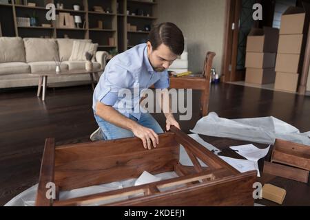 Young man engaged in assembling wooden furniture at home Stock Photo