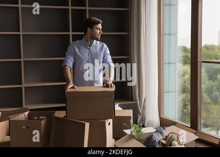 Man resting on relocation day standing indoor near stacked boxes Stock Photo