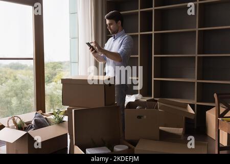 Man standing near cardboard boxes using smartphone on relocation day Stock Photo