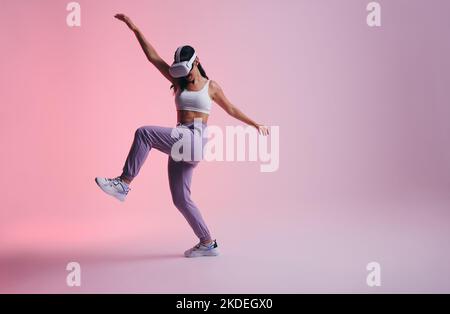 Active young woman dancing in the metaverse. Cheerful young woman enjoying herself while wearing virtual reality goggles. Woman having fun while explo Stock Photo