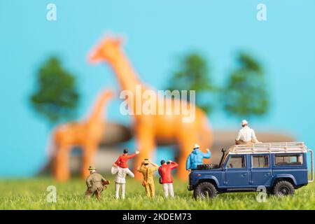 Miniature toys of a group of people on safari trip watching giraffes - a hunter, father and son on shoulder ride, photographer with an off road transp Stock Photo