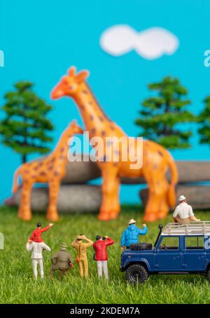 Miniature toys of a group of people on safari trip watching giraffes - a hunter, father and son on shoulder ride, photographer with an off road transp Stock Photo