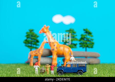 Miniature toys of a group of people on safari trip watching giraffes - a hunter, father and son on shoulder ride, photographer with an off road transp Stock Photo