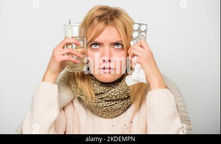Flu home remedies. Woman wear warm scarf because illness or flu. Girl hold glass water tablets and thermometer light background close up. Get rid of Stock Photo