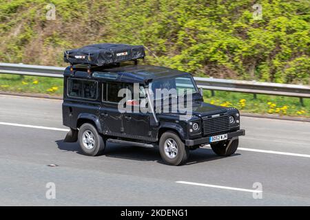 2002 Black Land Rover Defender 110 Td5 Xs LCV Station Wagon SWB travelling on the M6 Motorway UK with Tentbox attached to roof rack. Stock Photo