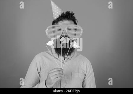 Guy in party hat celebrate, posing with photo props. Hipster in giant sunglasses celebrating. Emotional diversity concept. Man with beard on cheerful Stock Photo