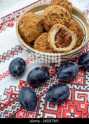 sweet plum dumplings made of leavened dough and fresh plums on clay bowl and plums aside Stock Photo
