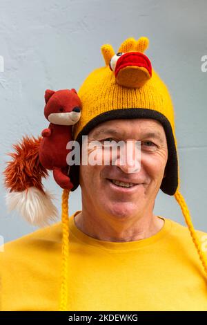 Man wearing yellow fox and chicken hat at Bridport Hat Festival, Dorset UK in September Stock Photo