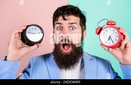 Man bearded hipster hold two different clocks. Guy unshaven puzzled face having problems with changing time. Time zone. Changing time zones affect Stock Photo