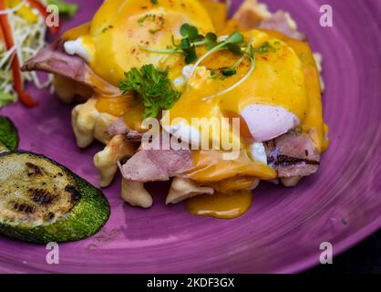 Eggs Benedict (poached eggs) on grilled ham with holland sauce on belgian waffles with grilled zucchini with plate of banana and cup of passion juic Stock Photo