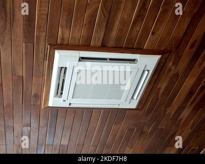 Ceiling mounted cassette type air conditioner system on wooden ceiling. White ceiling air conditioning decoration on wood plank background. Stock Photo