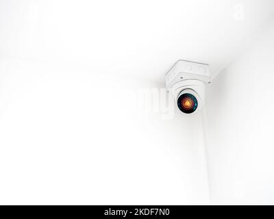 The digital eye technology on white security CCTV Camera or surveillance operating on ceiling in the corner room in the white wall building background Stock Photo