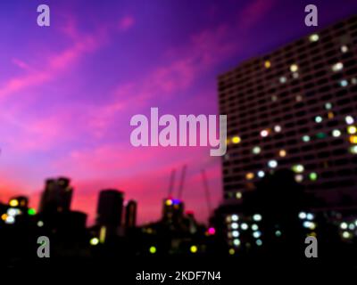 Blurred silhouette of building, cityscape on purple and blue sky background. Blurry colorful lights with business building on dark after sunset. Abstr Stock Photo
