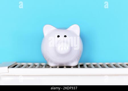 Concept for saving money for gas for heating with piggy bank on radiator in front of blue background Stock Photo