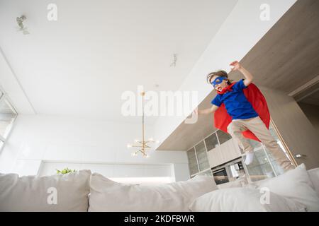 Very excited little girl dressed like superhero jumping alongside the living room Stock Photo