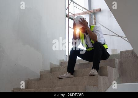 Stressed Architect man sitting on stair at construction site, green energy concept Stock Photo