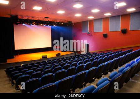 A large empty conference hall with blue empty seats, illuminated lights and a presentation screen Stock Photo