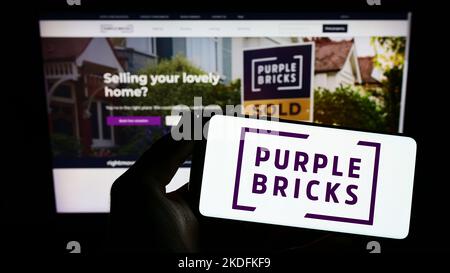 Person holding smartphone with logo of real estate company Purplebricks Group plc on screen in front of website. Focus on phone display.