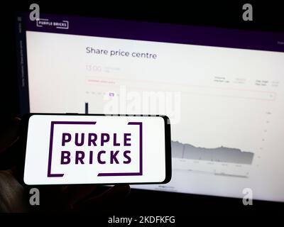 Person holding mobile phone with logo of real estate company Purplebricks Group plc on screen in front of web page. Focus on phone display.