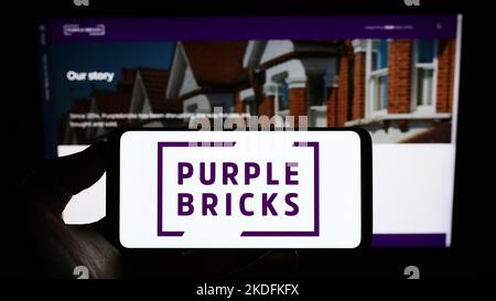 Person holding cellphone with logo of real estate company Purplebricks Group plc on screen in front of business webpage. Focus on phone display.