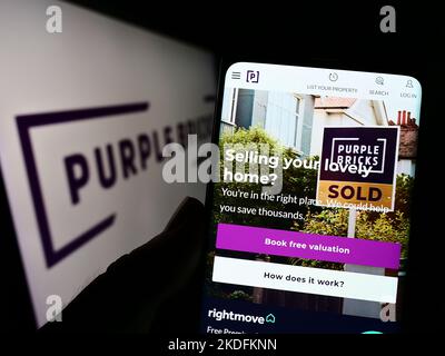 Person holding cellphone with website of real estate company Purplebricks Group plc on screen in front of logo. Focus on center of phone display.