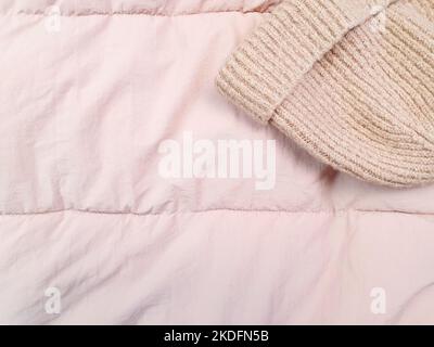 pink knitted hat and down jacket fabric background, pink puffer jacket texture. Top view Stock Photo
