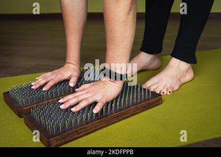 A woman practicing yoga, performs exercises on a sadhu board with nails, leans on nails with her hands, a concept on the theme of a healthy lifestyle Stock Photo