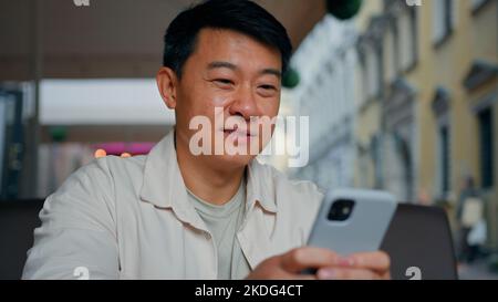 Close-up happy asian man holding mobile phone browsing social network male tourist booking ticket using smartphone sends email message communicates in Stock Photo
