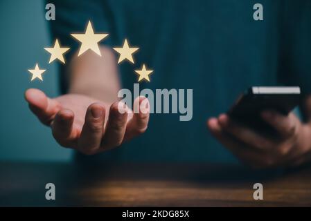 Young man using smartphone giving positive five stars rating review for client's satisfaction service surveys, Customer evaluation feedback concept. Stock Photo