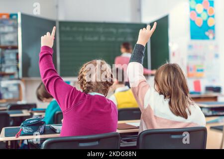 Two girl students raising hands to answer a question in school class Stock Photo