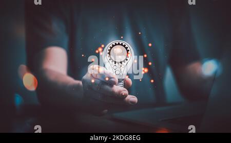 Man hand using computer and holding light bulb with a gear icon in it , The idea of ​​inspiration from online technology. innovation idea concept. Stock Photo