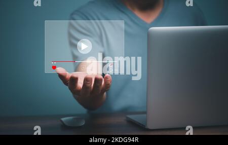 Young man using laptop computer with hand holding virtual playing video streaming screen icon, future screen technology concept. Stock Photo