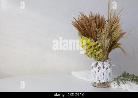 Scandinavian minimalist arrangement with dried flowers in a macrame vase on a white table Stock Photo