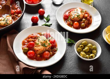 Cod stew with chickpeas, cherry tomatoes and olives on plate over dark stone background. Stock Photo