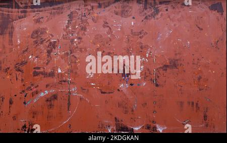 Front view of a messy, dirty and weathered plywood wall painted in red with stains from graffiti removal. Abstract full frame textured background. Stock Photo