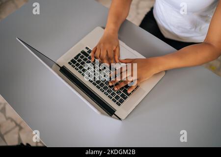 Close-up top view of unrecognizable African-American business woman using typing on laptop notebook keyboard sitting at home office desk. Stock Photo