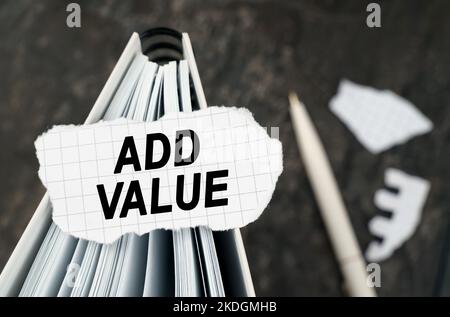On the table is a notebook on which lies a piece of torn paper with the inscription - Add Value. The pen lies outside the sharpness zone. Stock Photo