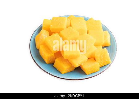 Dried and candied mango cubes on blue plate isolated on white background. Side view, close up, vegan, vegetarian food concept. Stock Photo